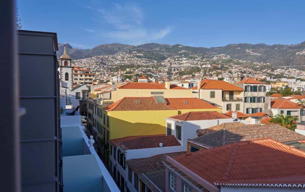 Rooftops of colorful buildings with mountains covered in city sprawl in the background.