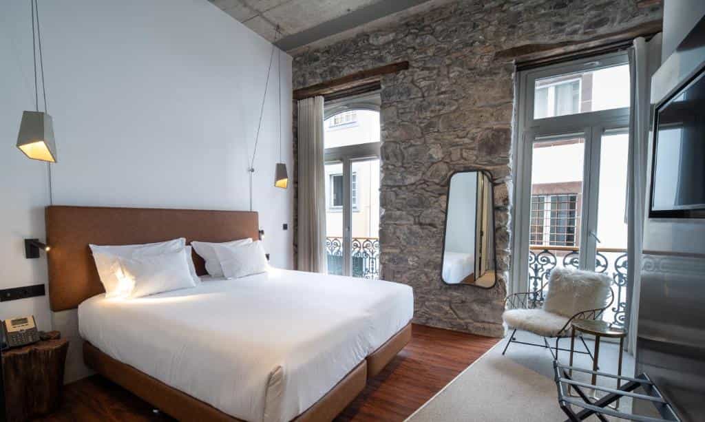 Hotel bedroom with white linens, exposed stone wall, and balcony view at Le Petit Hotel.
