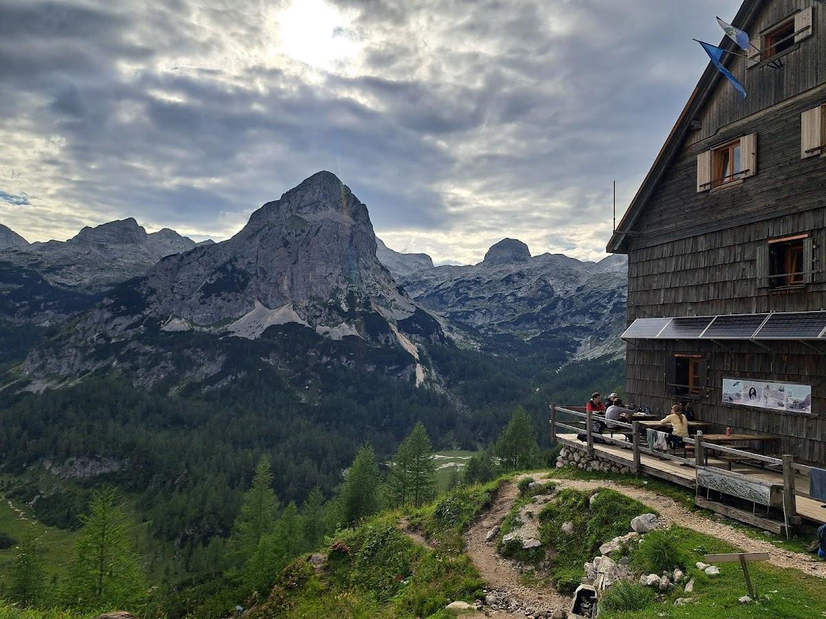 Hikers resting on wooden deck of mountain hut overlooking rocky peaks and forested valley