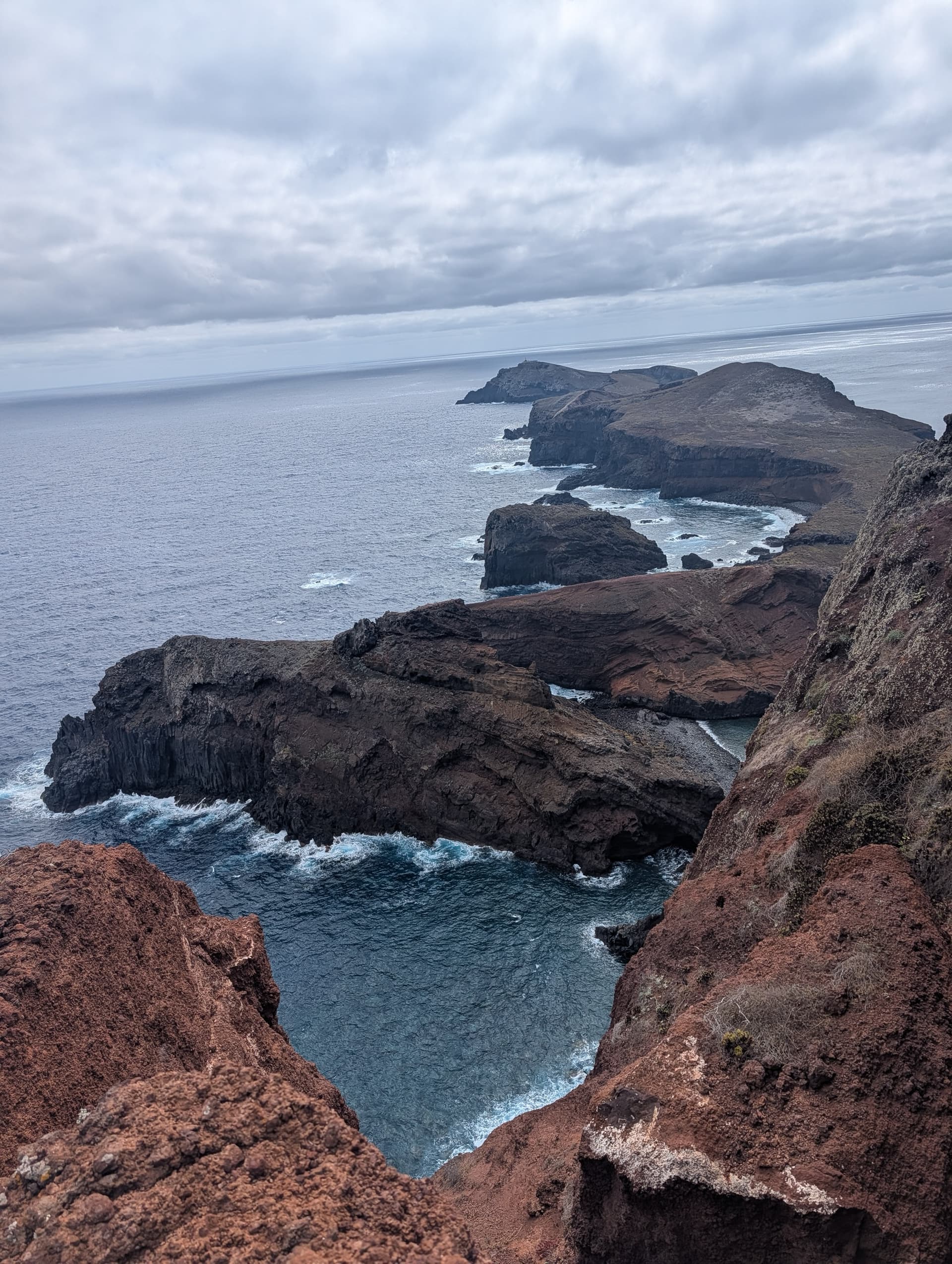 Sea stacks below volcanic cliffs along a rugged ocean coastline under a cloudy sky