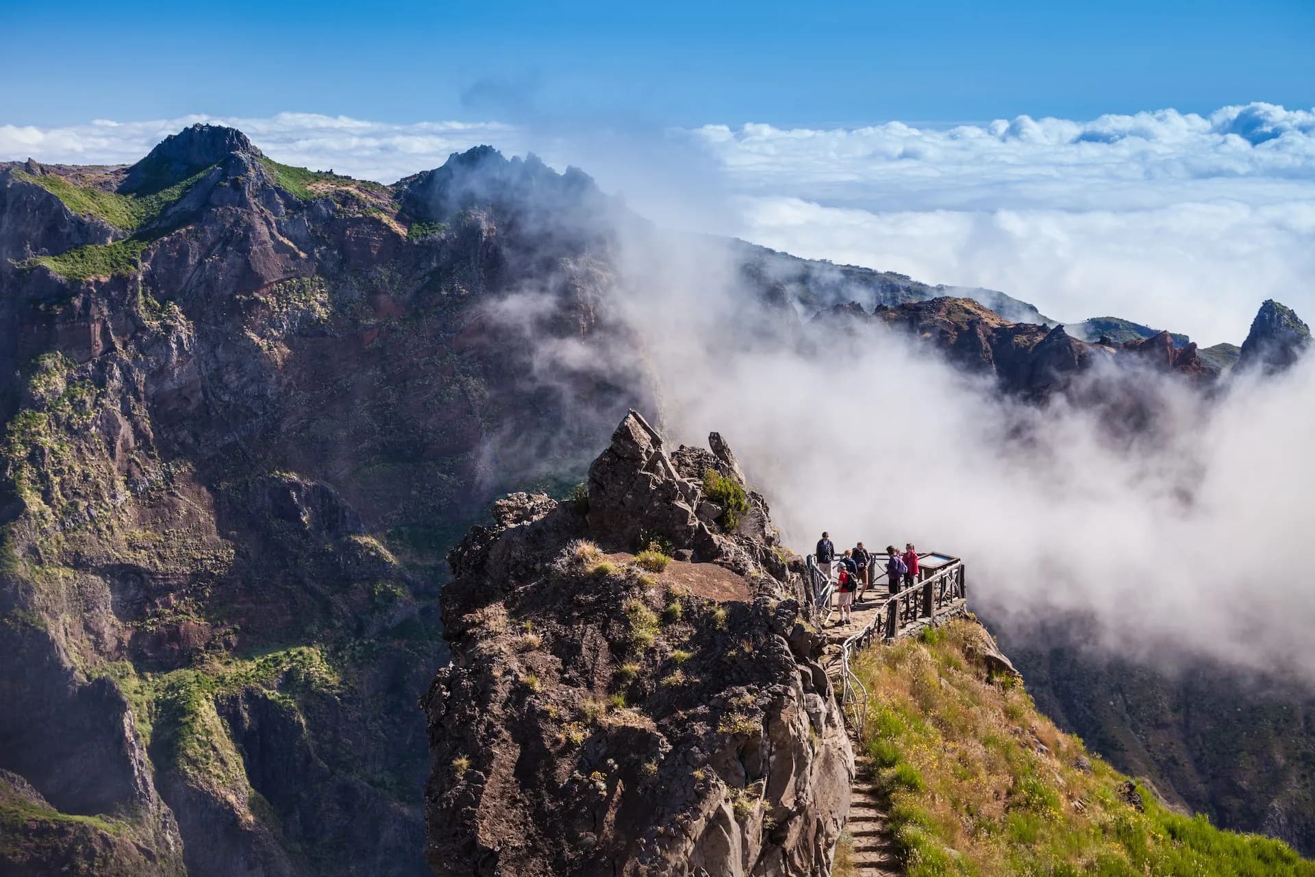Hikers on viewing platform above clouds on rugged peaks from Pico do Arieiro to Pico Ruivo.