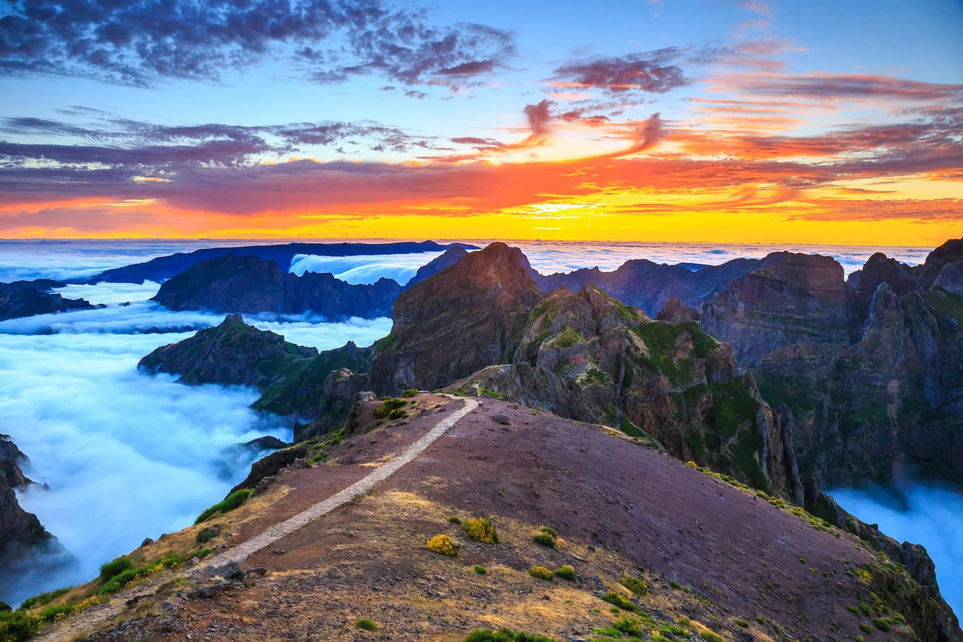 Hiking trail above clouds at sunrise over rugged mountains in Madeira.