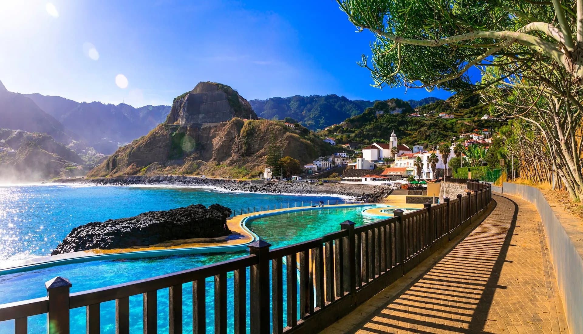Natural seawater swimming pools by the ocean with a village on a steep hillside in Porto da Cruz.