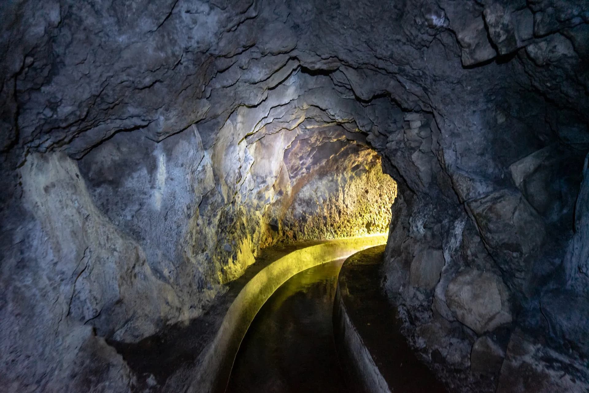 Tunnel on Levada do Norte with illuminated stone walkway curving through dark rock.