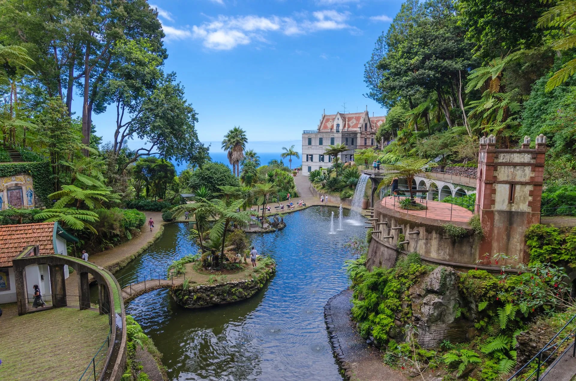 Lush tropical gardens with ponds, waterfalls, and a historic building overlooking the sea in Funchal.
