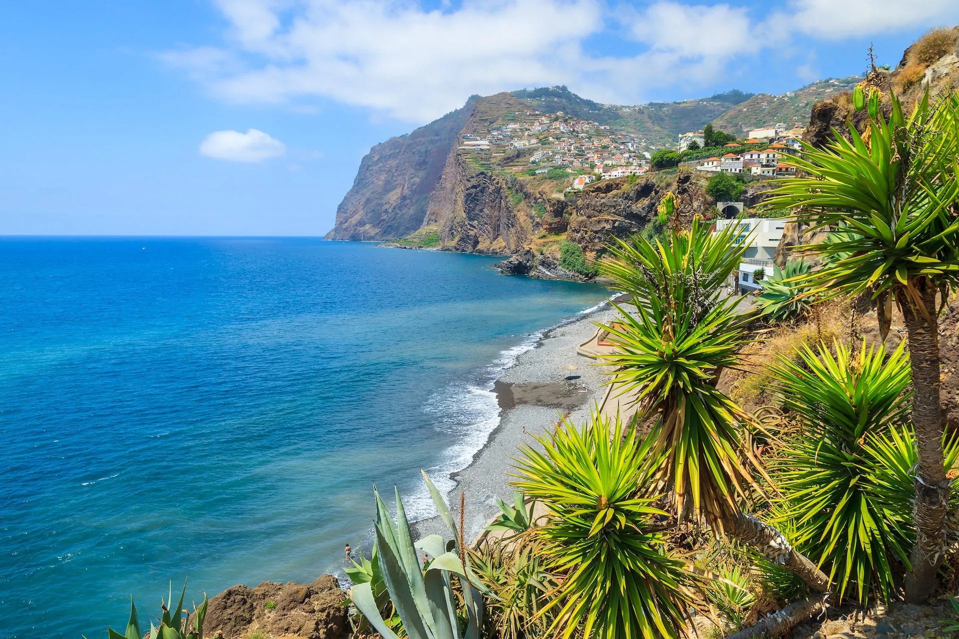 Coastal view of Cabo Girao with steep cliffs, town on hillside, and blue ocean water.