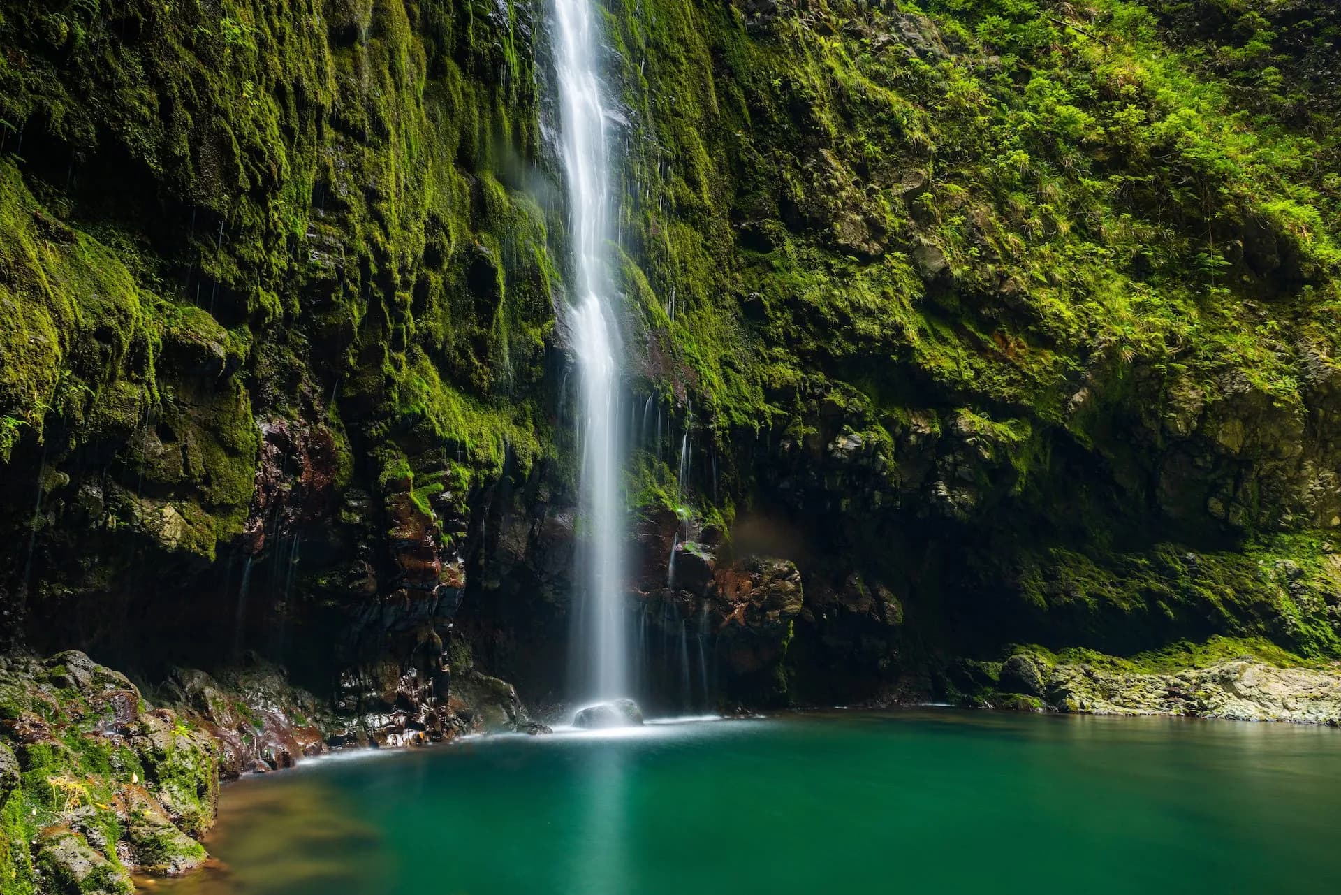 Waterfall cascading down moss-covered rocks into a deep green pool at Caldeirão Verde.
