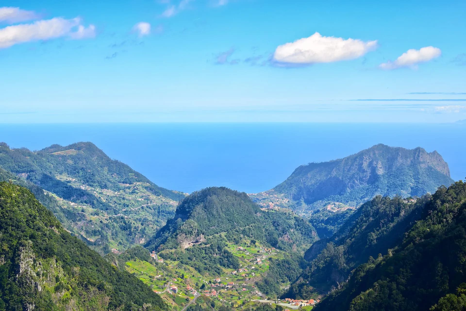 View from Vereda dos Balcões showing lush green mountains, scattered villages, and the blue ocean horizon.
