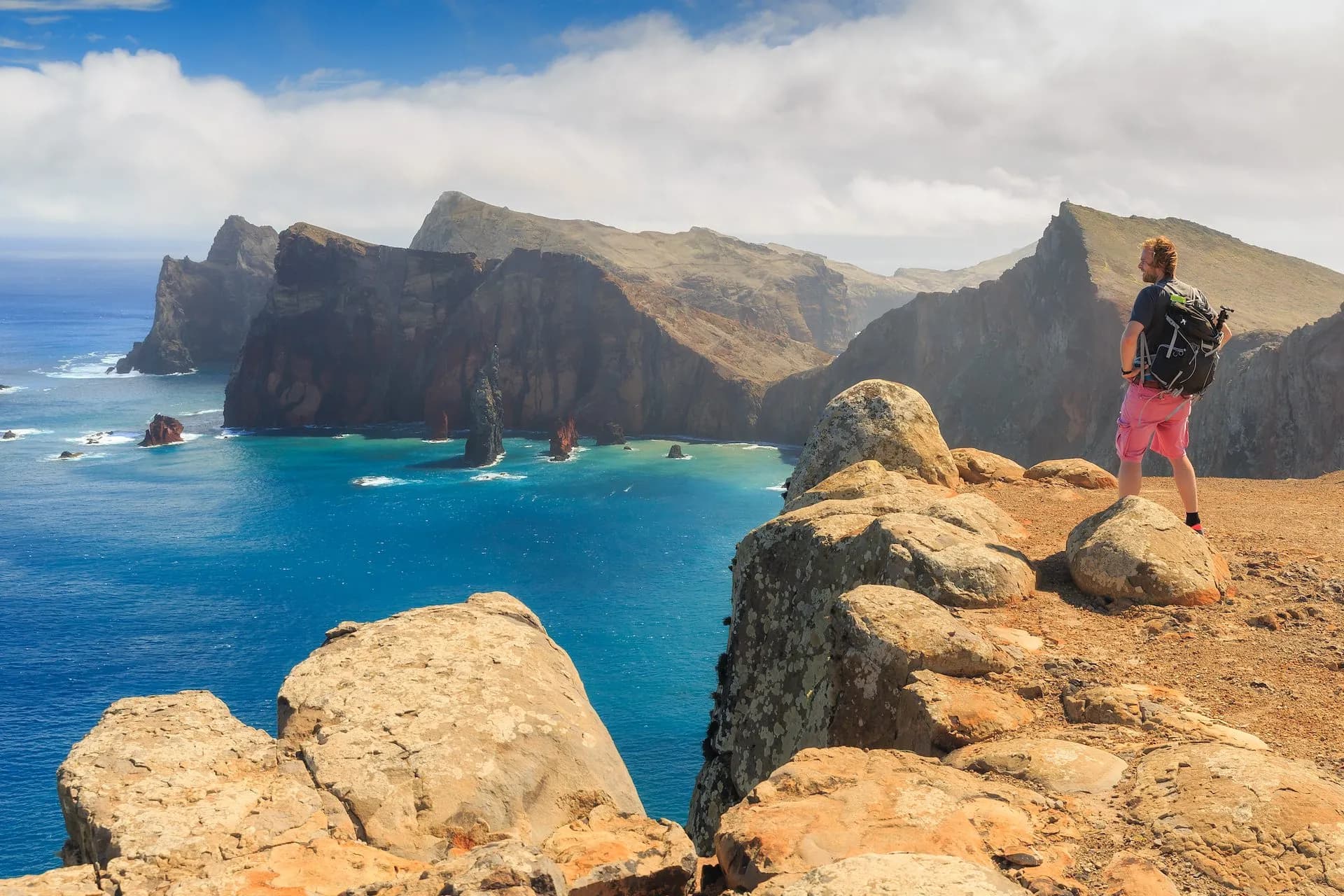 Hiker with backpack overlooking steep cliffs and turquoise sea at Ponta de São Lourenço