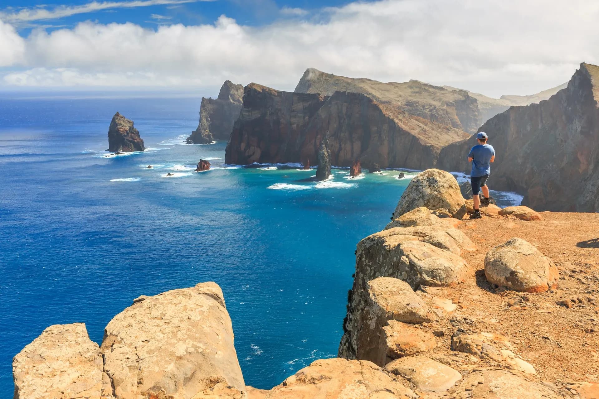 Hiker overlooking dramatic sea cliffs and turquoise water at Ponta do São Lourenço.