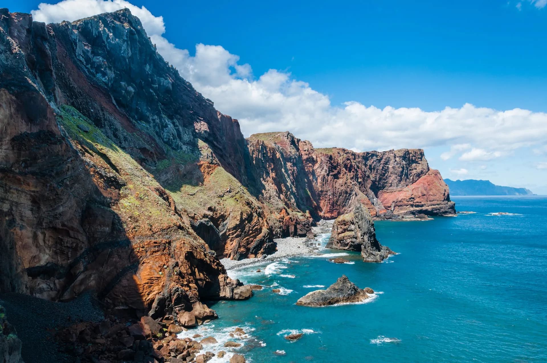 Cliffs of Ponta de São Lourenço with rugged red rock meeting turquoise ocean under blue sky.